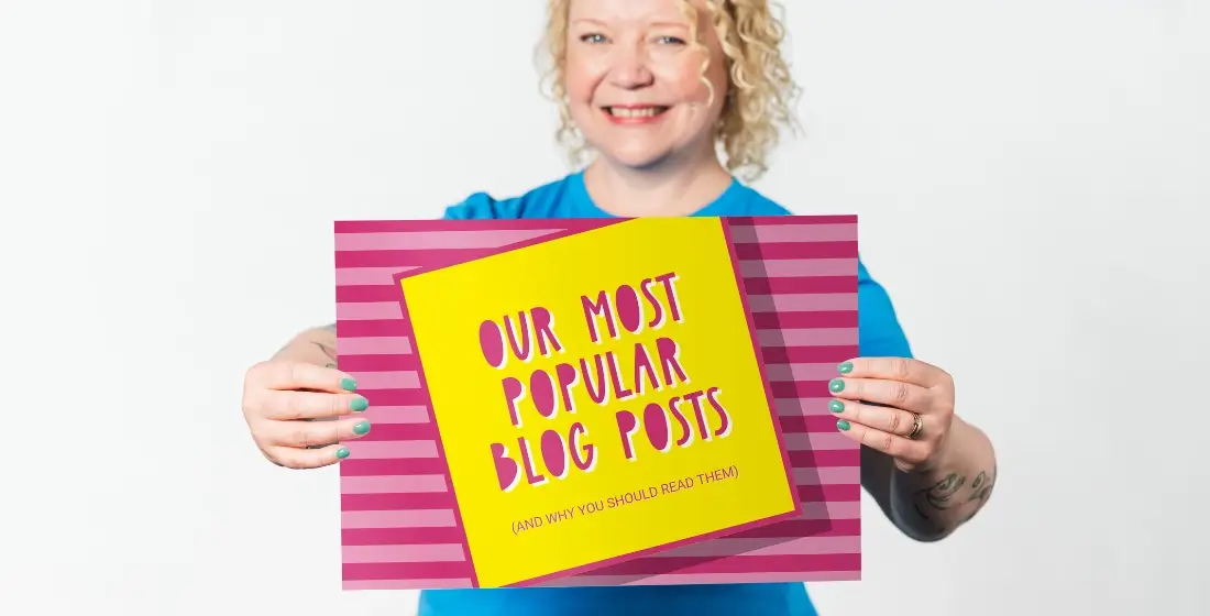 Helen Bee from B Double E holding an A3 card that says 'our most popular blog posts'. Helen is standing infront of a white background wearing a sky blue t-shirt, the sign is bright pink.