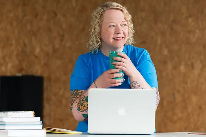 Helen Bee from B Double E sat behind an open laptop holding a mug looking to the right.