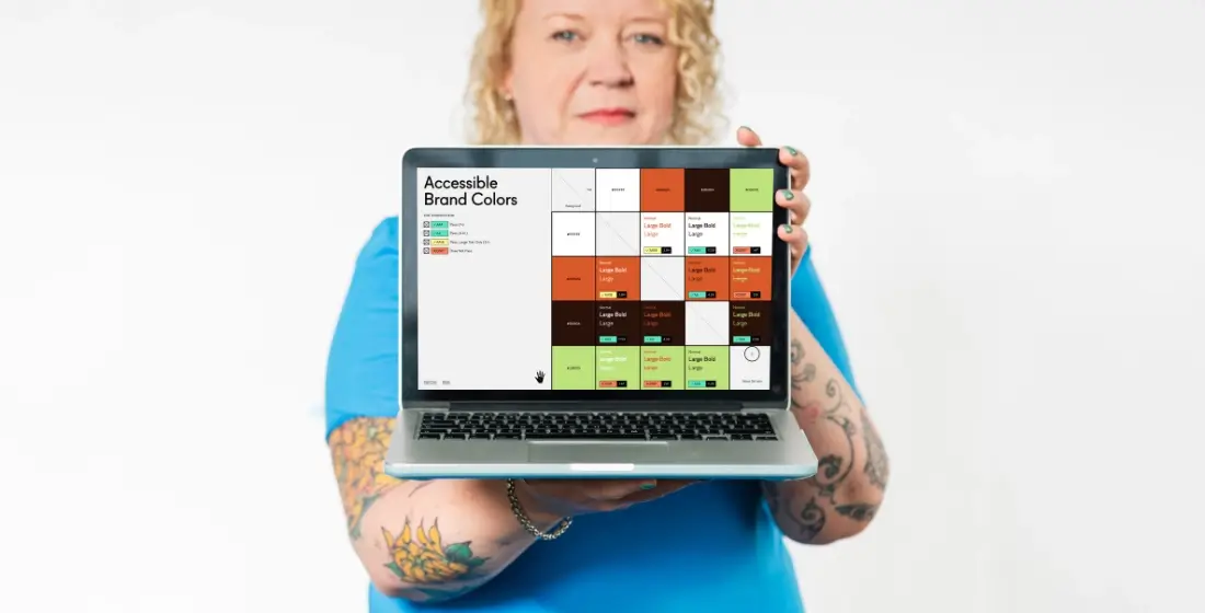 Helen Bee from B Double E holding a laptop with an online colour contrast checker showing various colours.